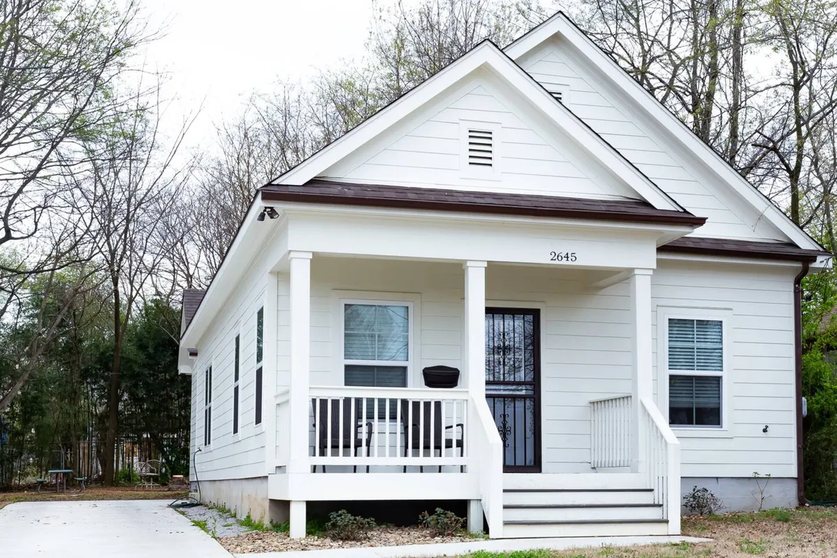 The image showcases the inviting exterior of a single-family house in Memphis, Tennessee, featuring a crisp white facade, a spacious front porch with comfortable seating, and a beautifully landscaped yard. The scene evokes relaxation and outdoor enjoyment, with spaces perfect for sipping morning coffee, socializing with friends, or unwinding as the sun sets.