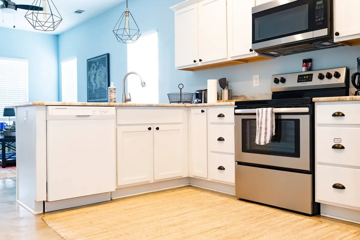 A bright, spacious kitchen featuring white cabinetry, gleaming stainless steel appliances, and a generous kitchen island. The setting is lively and welcoming, ideal for group cooking activities and family meals.