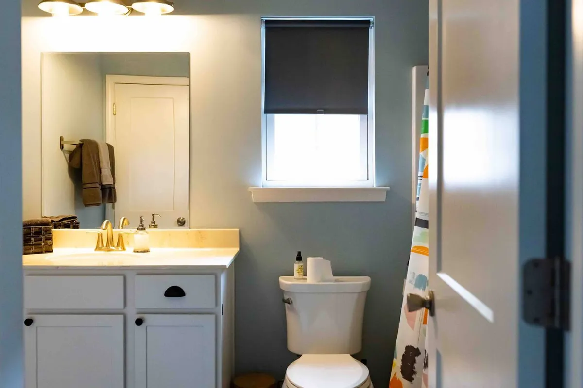 A modern bathroom with a bright window, metallic fixtures, a clean sink, a mirror, and a towel rack. The space is thoughtfully designed for comfort and daily routines.
