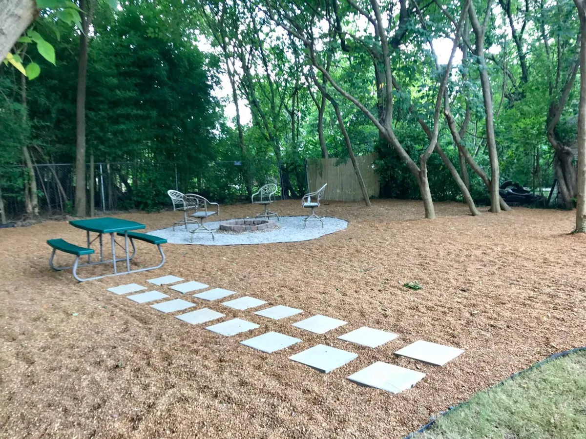An outdoor fire pit encircled by comfortable seating, with a gravel pathway leading to the space. The setting is relaxed, designed for communal campfire gatherings, storytelling, and stargazing under the night sky.