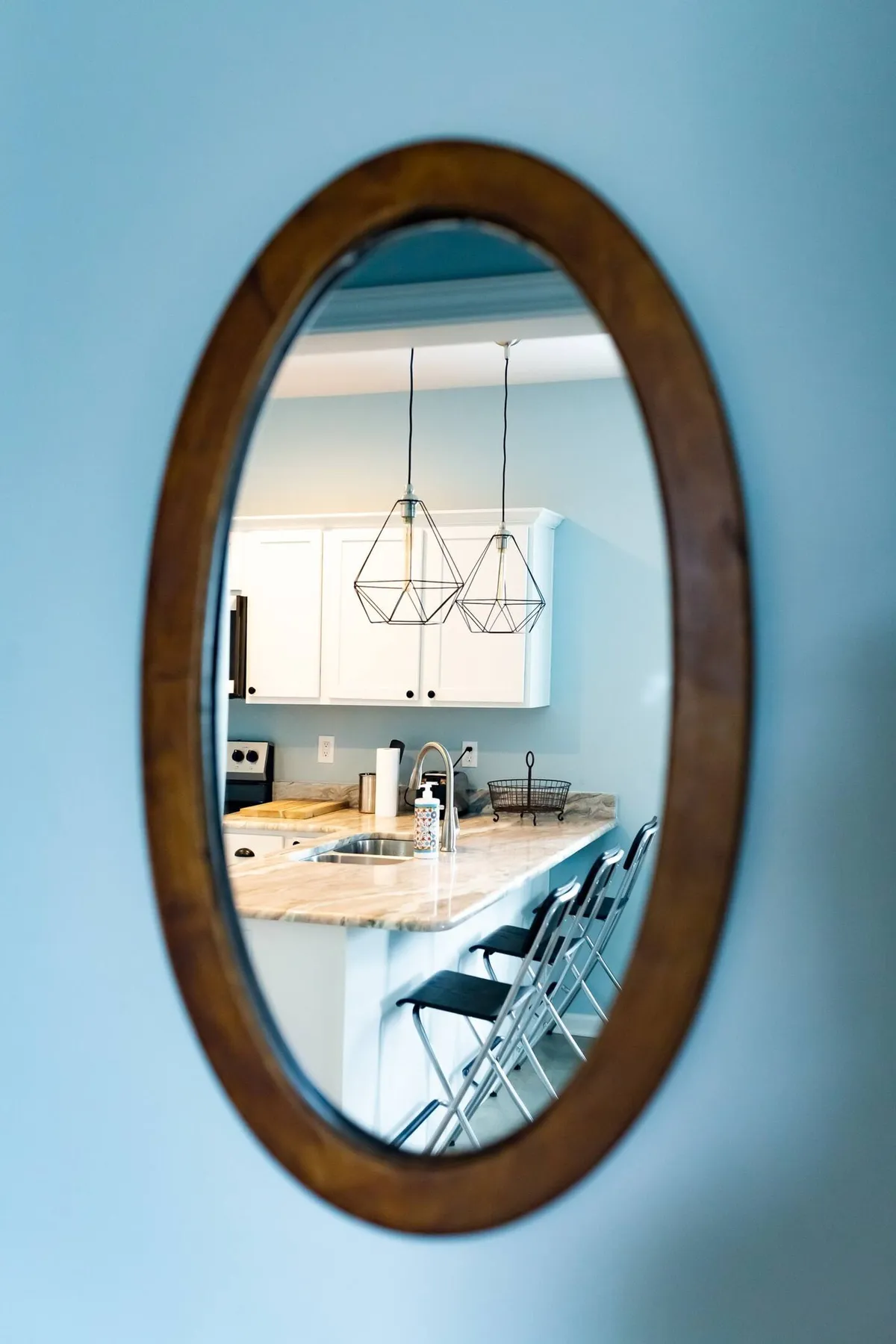 A cozy kitchen scene with an oval mirror above the counter, stylish hanging light fixtures, and a welcoming countertop space ideal for preparing meals and entertaining guests.