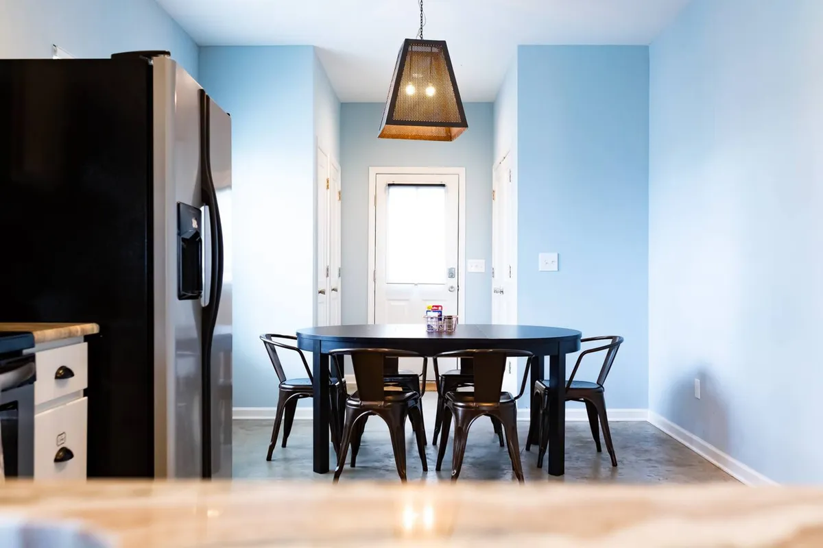 A cozy, inviting dining area with a wooden table, elegant light fixture, and black chairs arranged for group gatherings. The space exudes warmth and is designed for memorable meals and conversation.